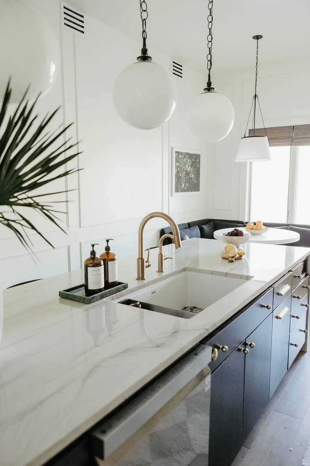View of the kitchen island sink area featuring a matte gold faucet, white marble countertop, and two oversized globe pendant lights.