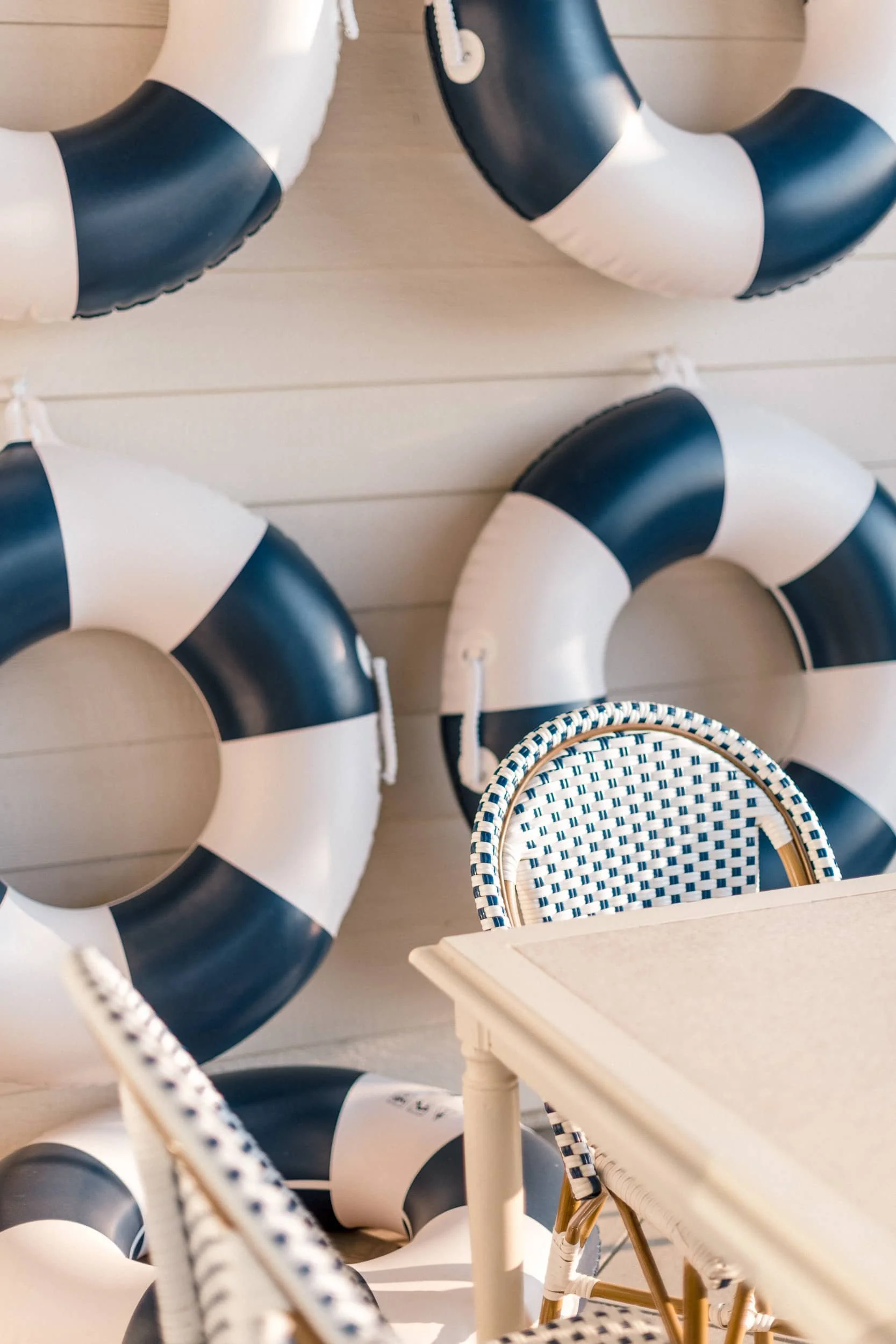 Tight close-up of the navy and white striped life preserver wall decor hanging on a white shiplap exterior wall, with a woven pattern chair back visible.