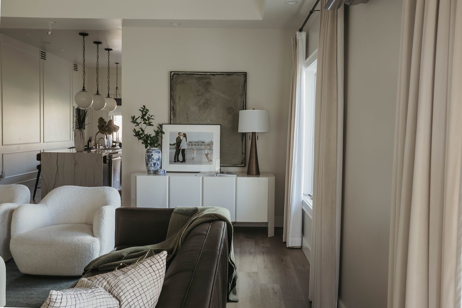 View of the open-concept living room showing the white credenza, a curved bouclé chair, and kitchen in the background.