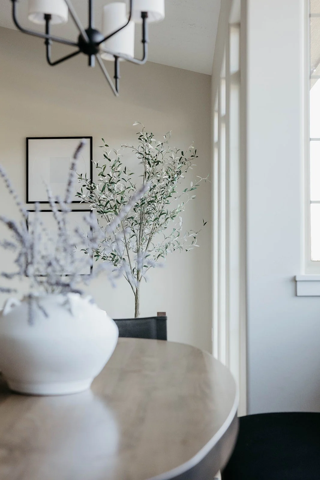 Close-up of a light round wood dining table styled with a white vase containing faux lavender and olive branches.