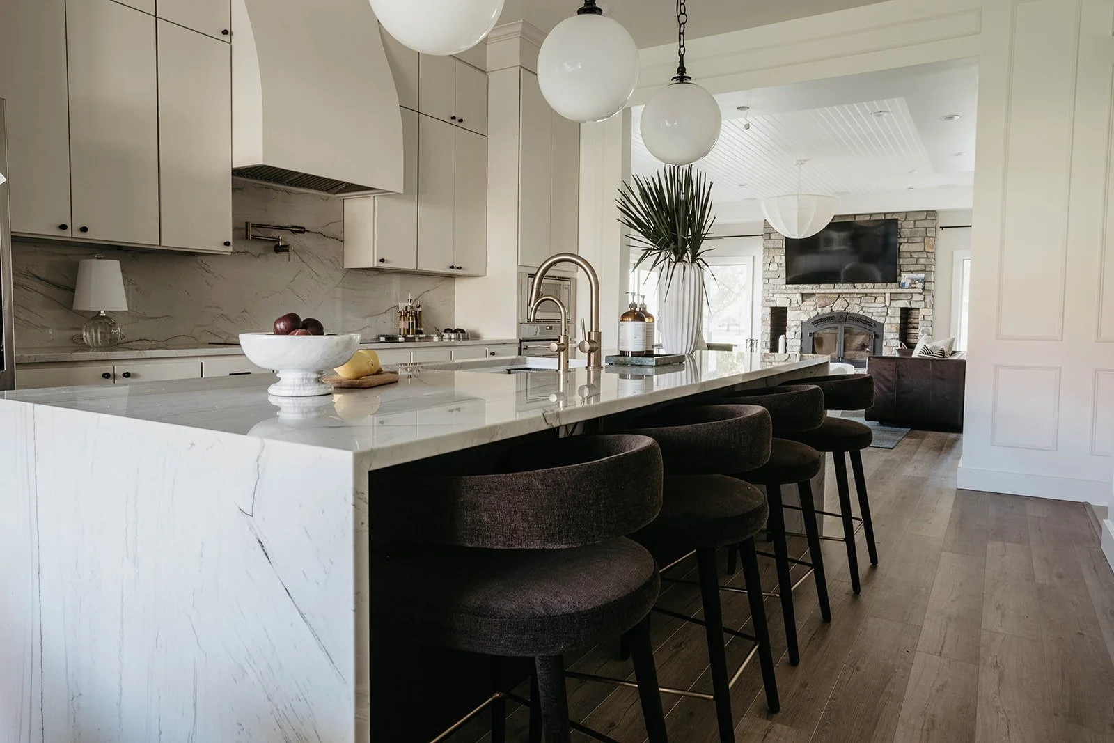 Kitchen island view featuring a row of dark charcoal-colored counter stools with brass footrests, pulled up to the marble island.