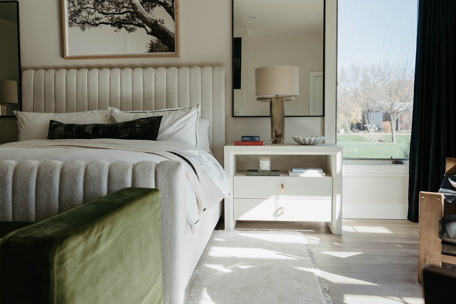 View of the master bedroom showing the white bedding, a white floating vanity or desk area, and bright light streaming in from the window.