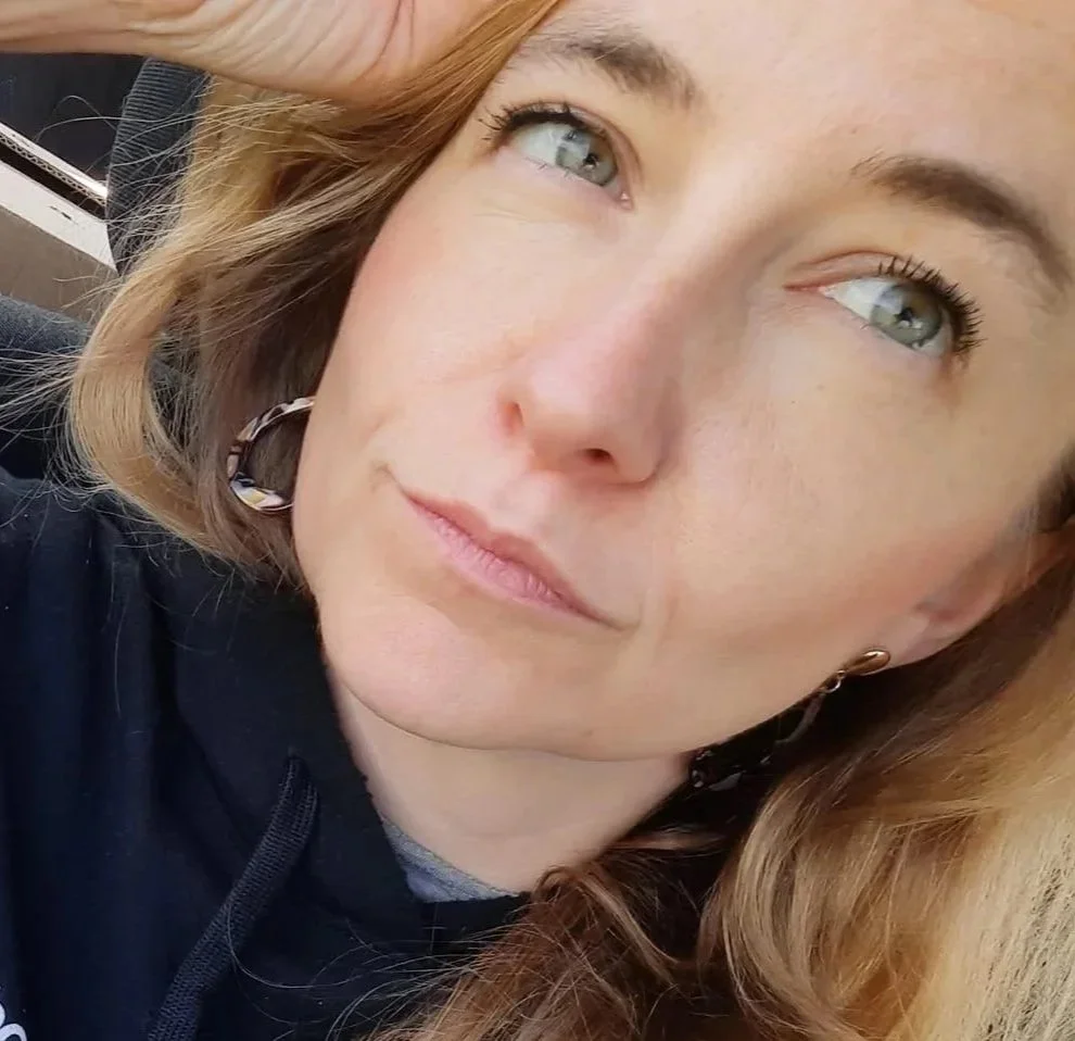 Nahaufnahme eines Mädchens mit blonden Haaren, blauen Augen und einem schwarzen Hoodie, das draußen sitzt.