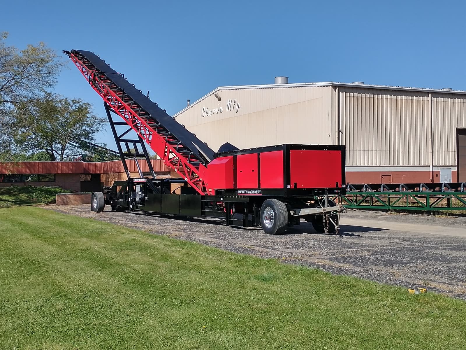 A red and black Infinity 8048 in front of Sharon Manufacturing Building with green grass and a blue sky.