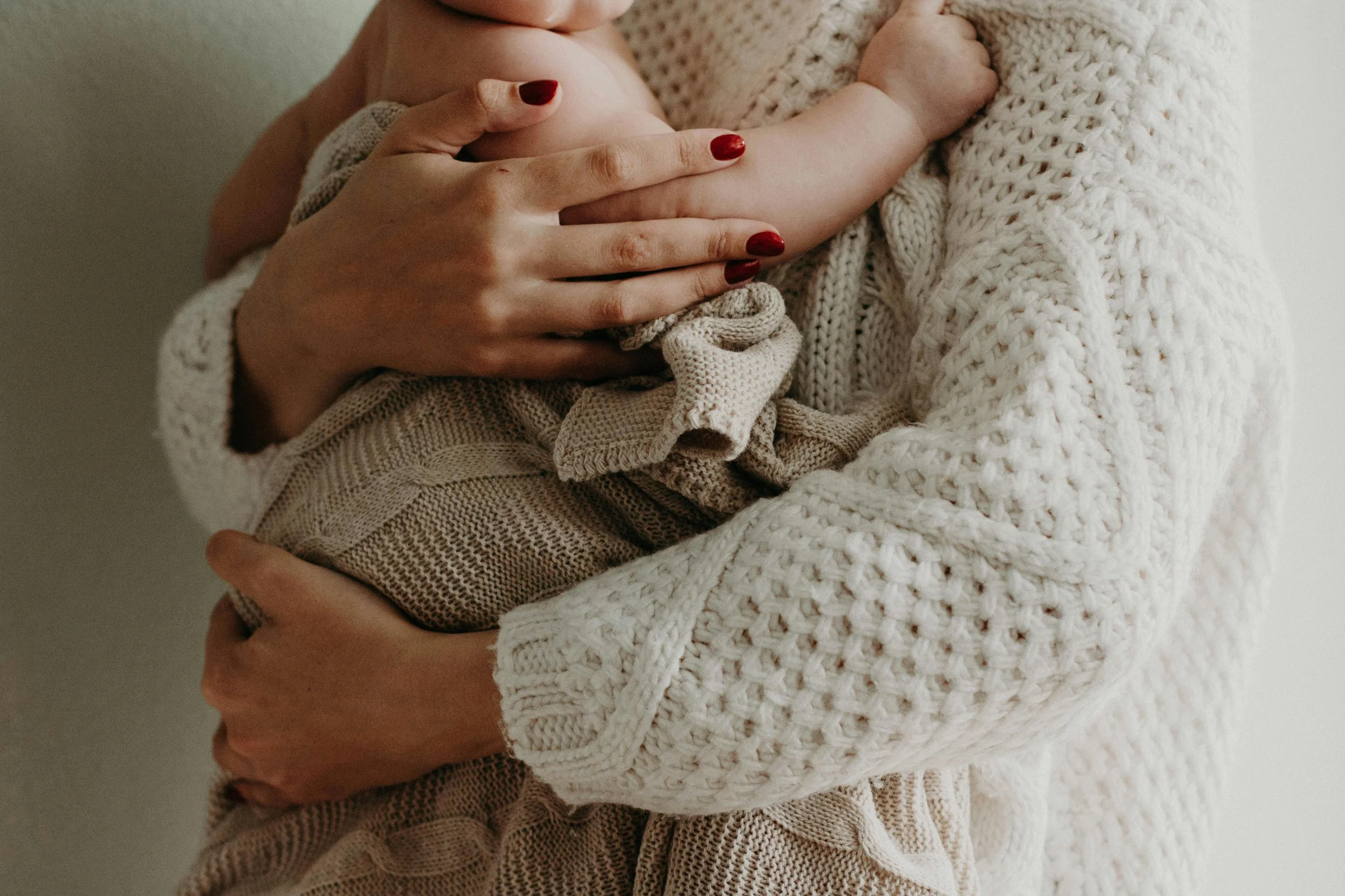 Woman with red nails holding a new baby in a sweater