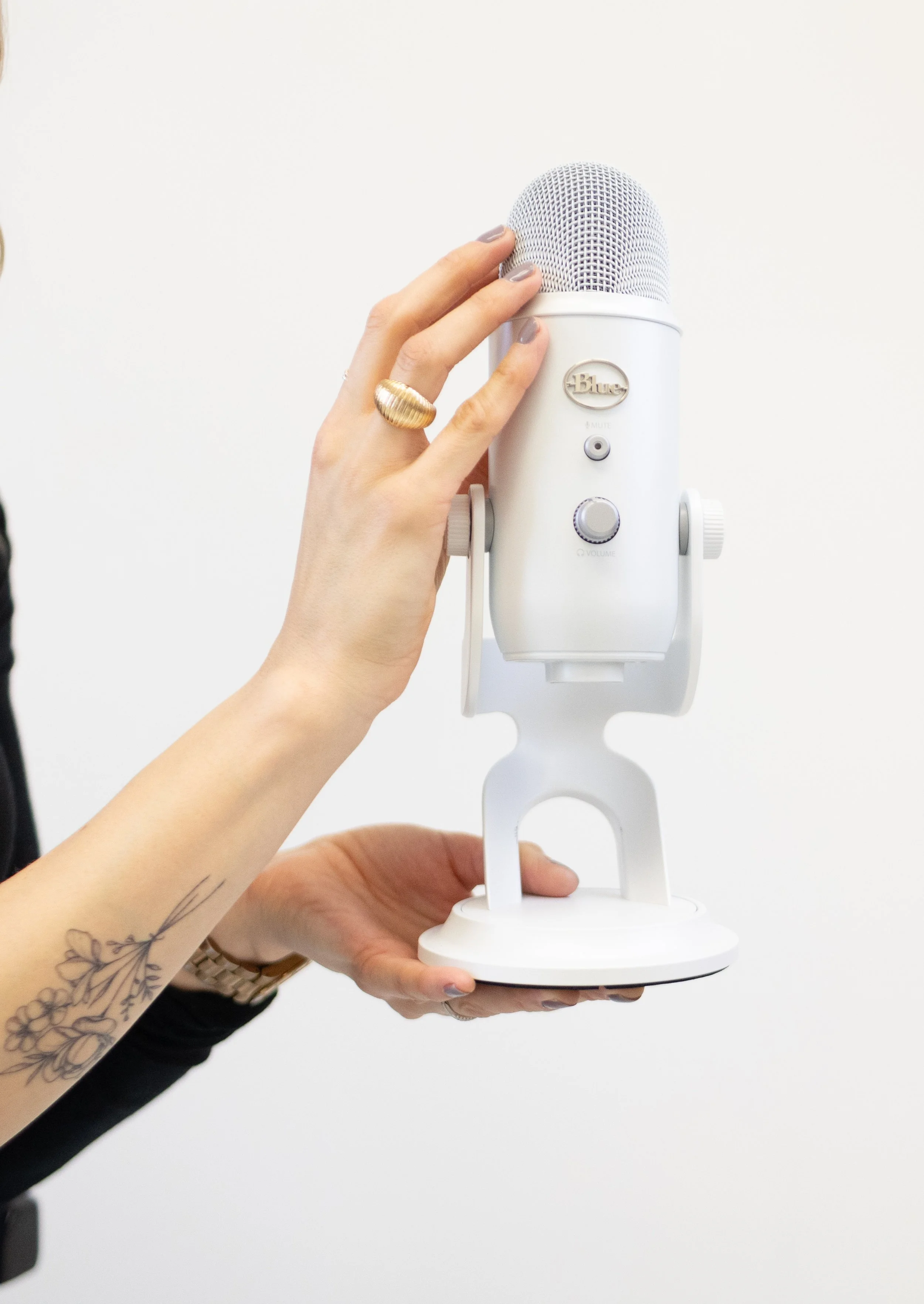 Person holding a white Blue Yeti microphone against a white background.