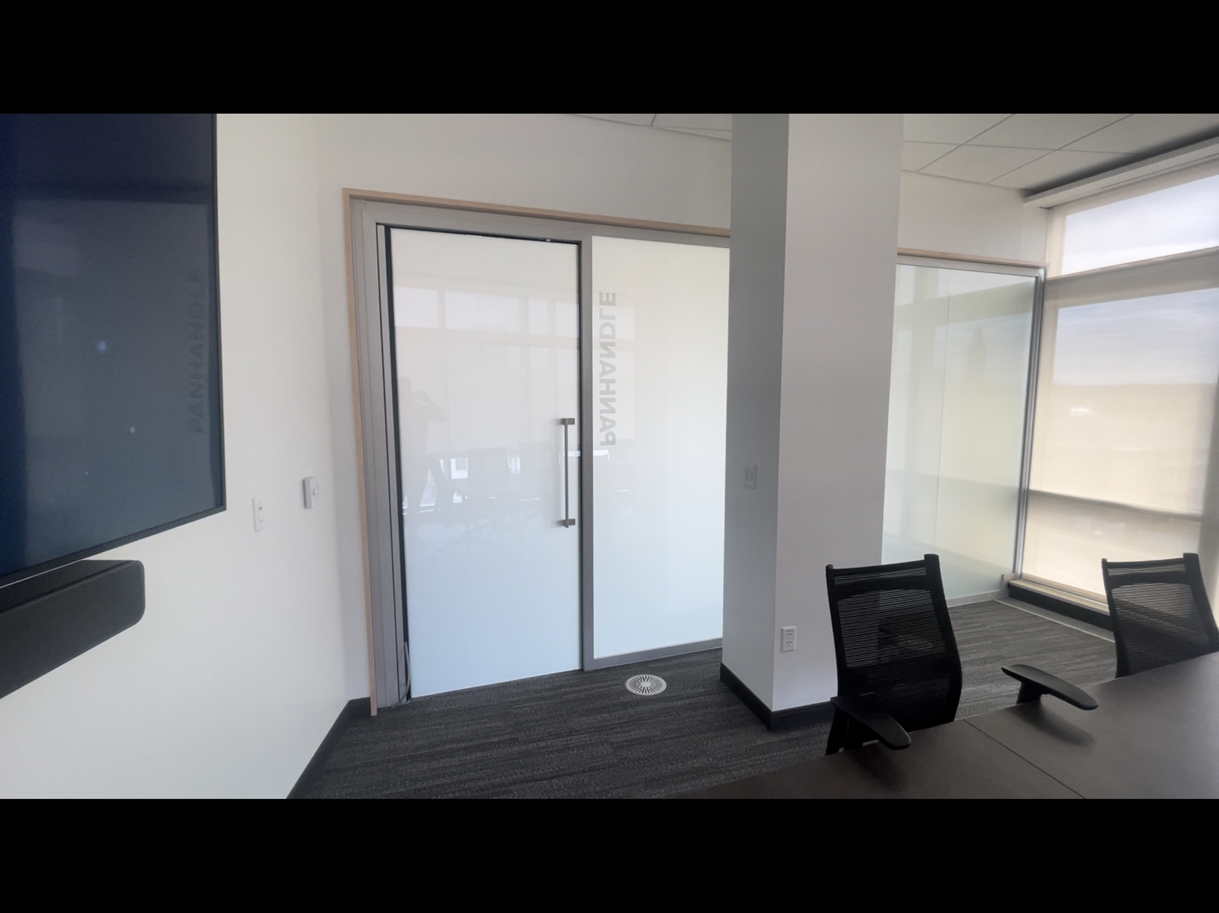 Modern conference room with glass door, black office chairs, and large windows with shades.Smart film powered on.