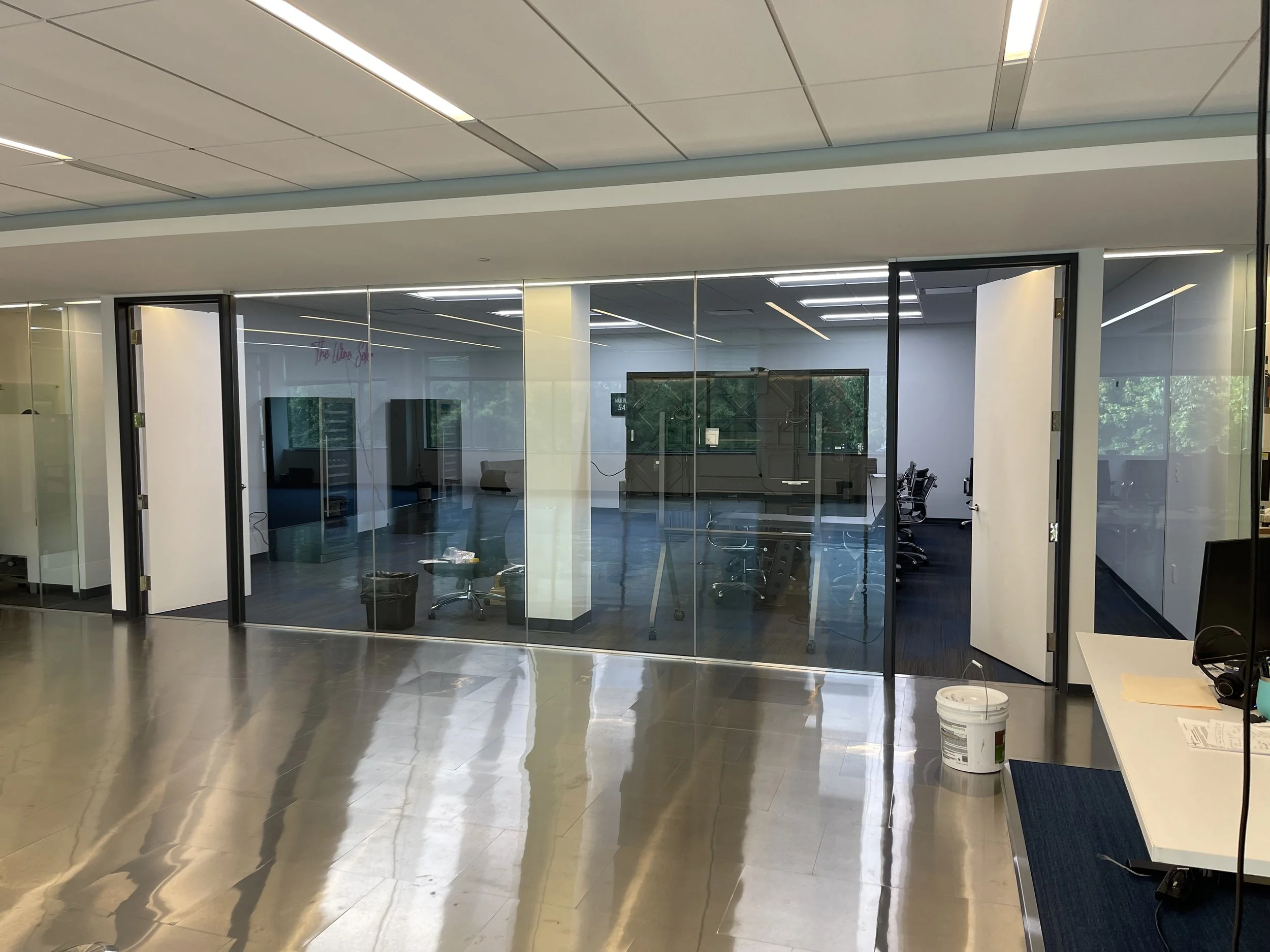 Empty office conference room with glass walls, chairs, and rowing machine, seen from the hallway.