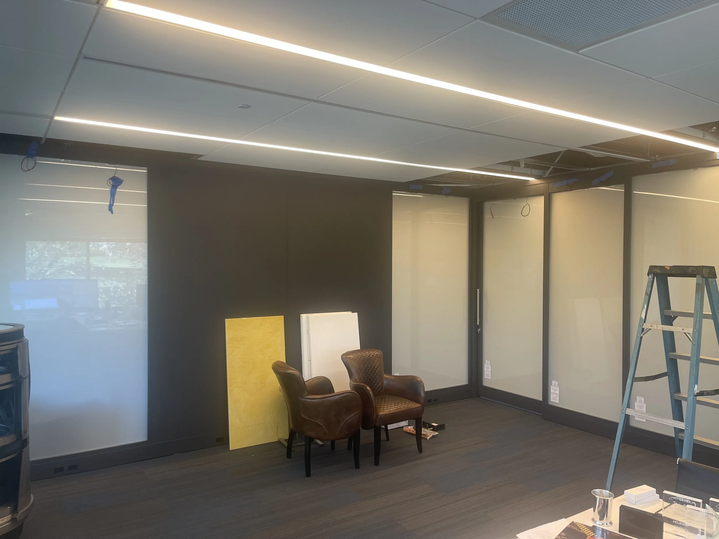 Office or conference room under construction with a ladder, chairs, construction materials, and partially installed glass walls.