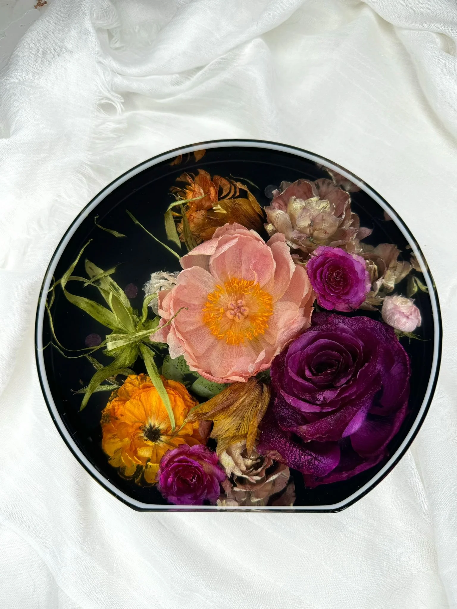 Freestanding circle l filled with floating assorted dried flowers, including pink, purple, yellow, and brown blossoms, placed on a white fabric background.