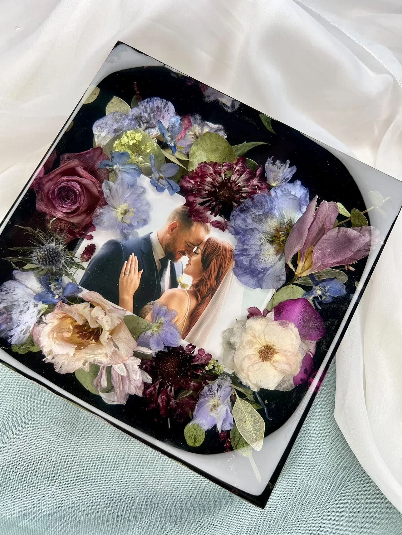 A decorative photo frame with a wedding picture of a bride and groom surrounded by real pressed flowers and leaves.