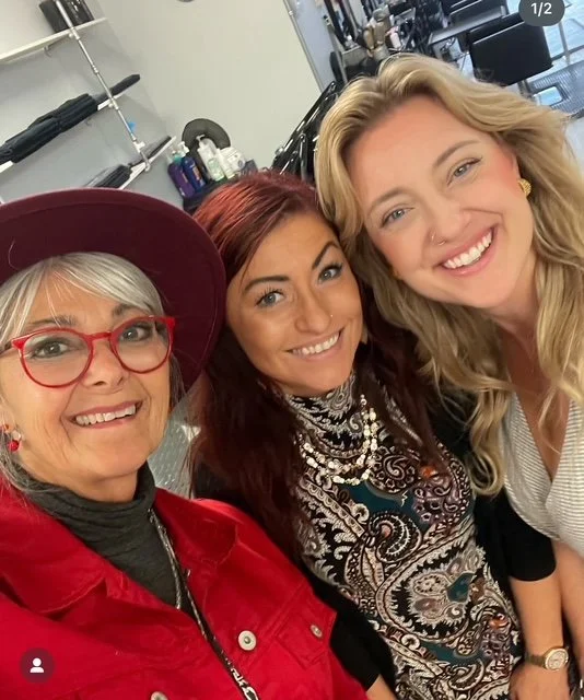 Three women smiling and taking a selfie in a salon or beauty shop setting.