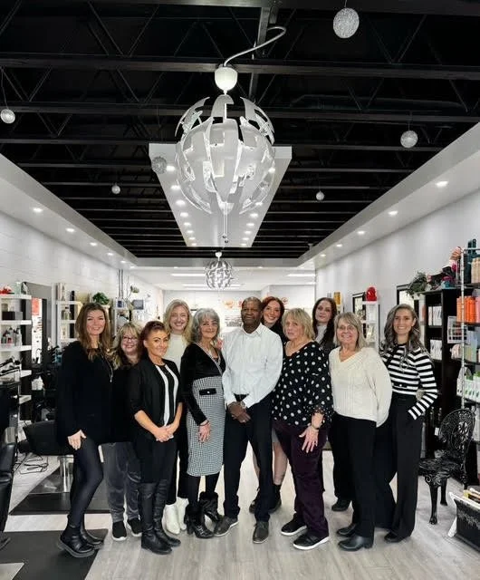 Group of people standing together in a retail store, smiling for the photo, with shelves of products behind them and modern ceiling lights overhead.