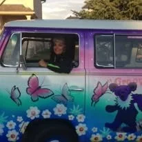 A colorful van decorated with butterfly and unicorn designs, with a woman smiling in the driver's seat.