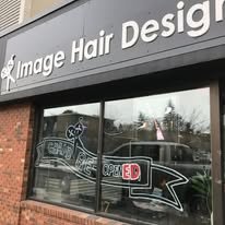 Storefront window displaying 'Image Hair Design' sign with a reflection of nearby cars and trees.