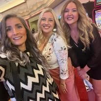 Three women smiling and posing together indoors, possibly at an event or gathering