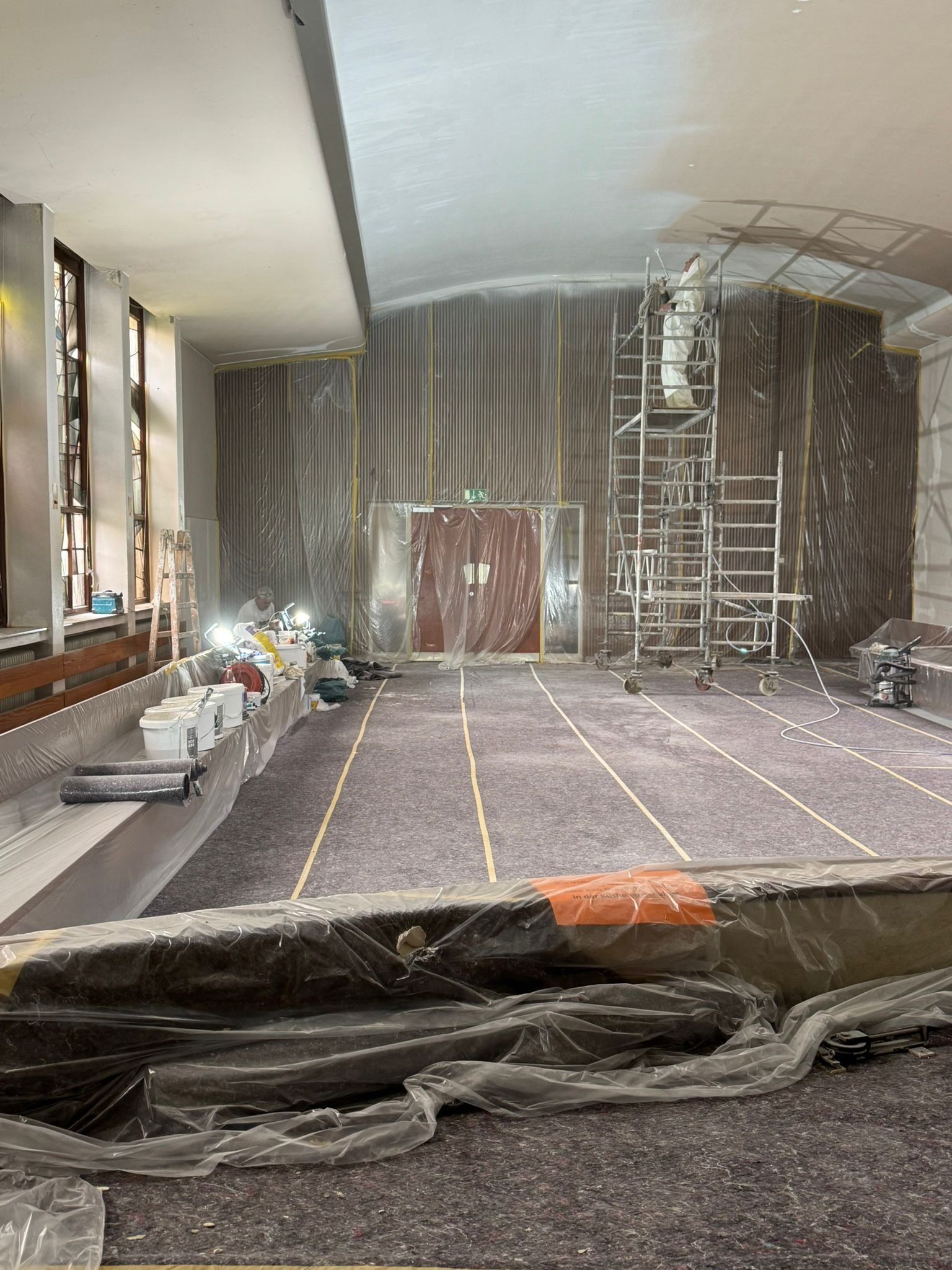 Innenansicht eines Raumumbaus mit Baugerüsten, Schutzfolie und Werkzeugen, vermutlich in einer Kirche oder Veranstaltungshalle.