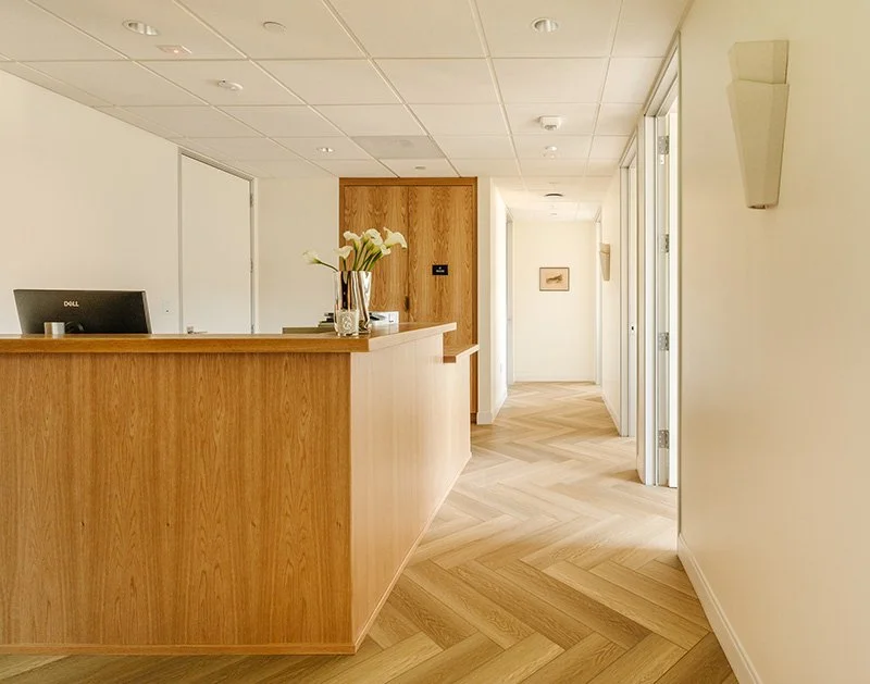 A photo of the interior of Wilshire Internal Medicine, showing the nurse's desk with white flowers and an elegant hallway with a herringboned wooden floor.