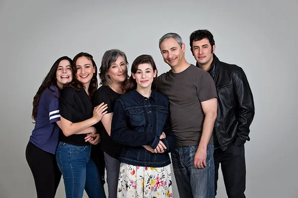 Six people standing together in front of a plain gray background, smiling and posing for the camera.