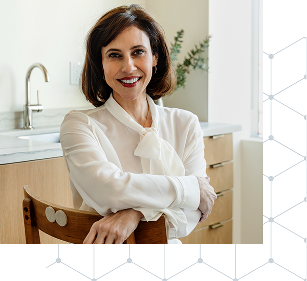 Dr Meszaros smiling, sitting in a chair wearing a white blouse.