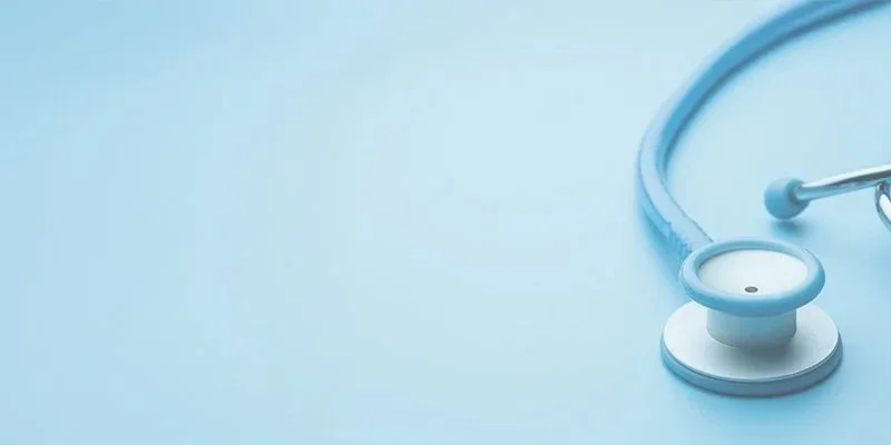 Light blue stethoscope with earbuds and chest piece on a light blue background.