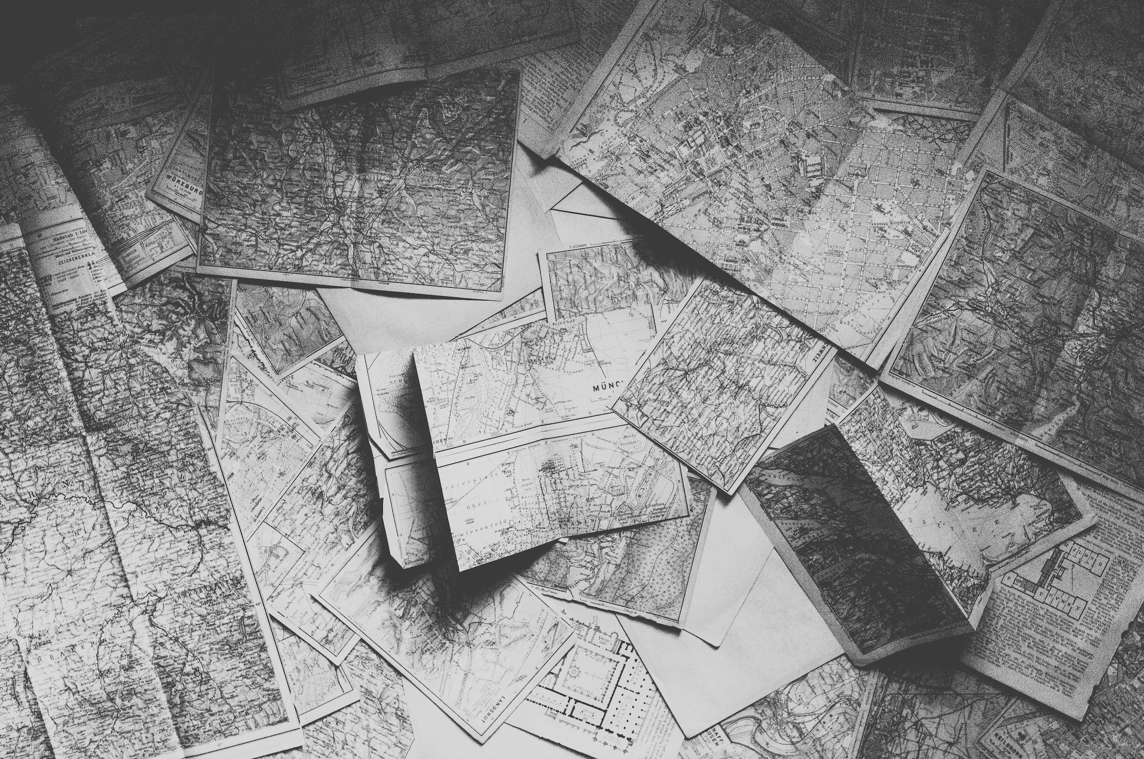 A scattered collection of black-and-white maps and city plans overlapping each other on a surface.