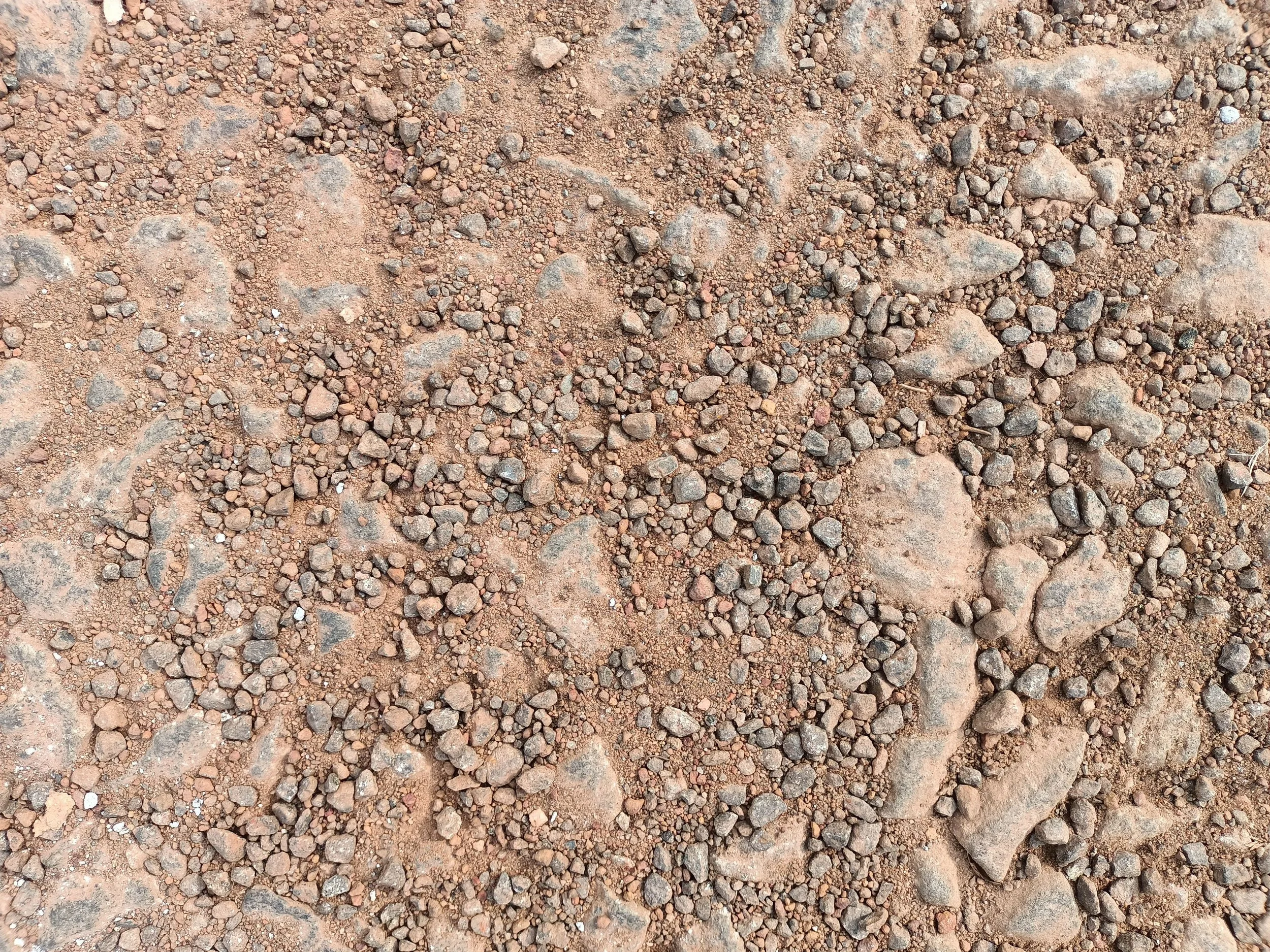 A close-up view of a dirt ground with small rocks and pebbles scattered across the surface.