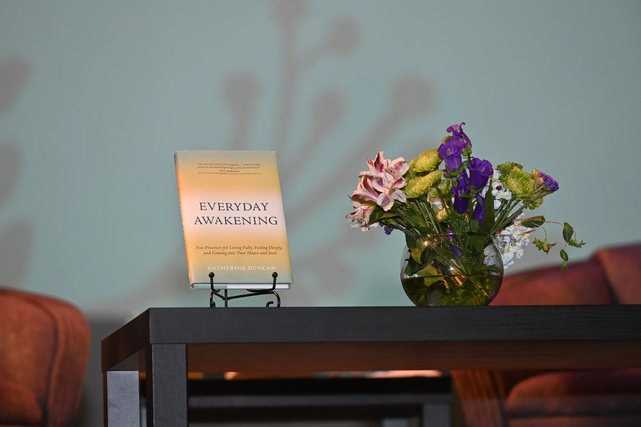 Book titled Everyday Awakening on a stand next next to a vase of flowers