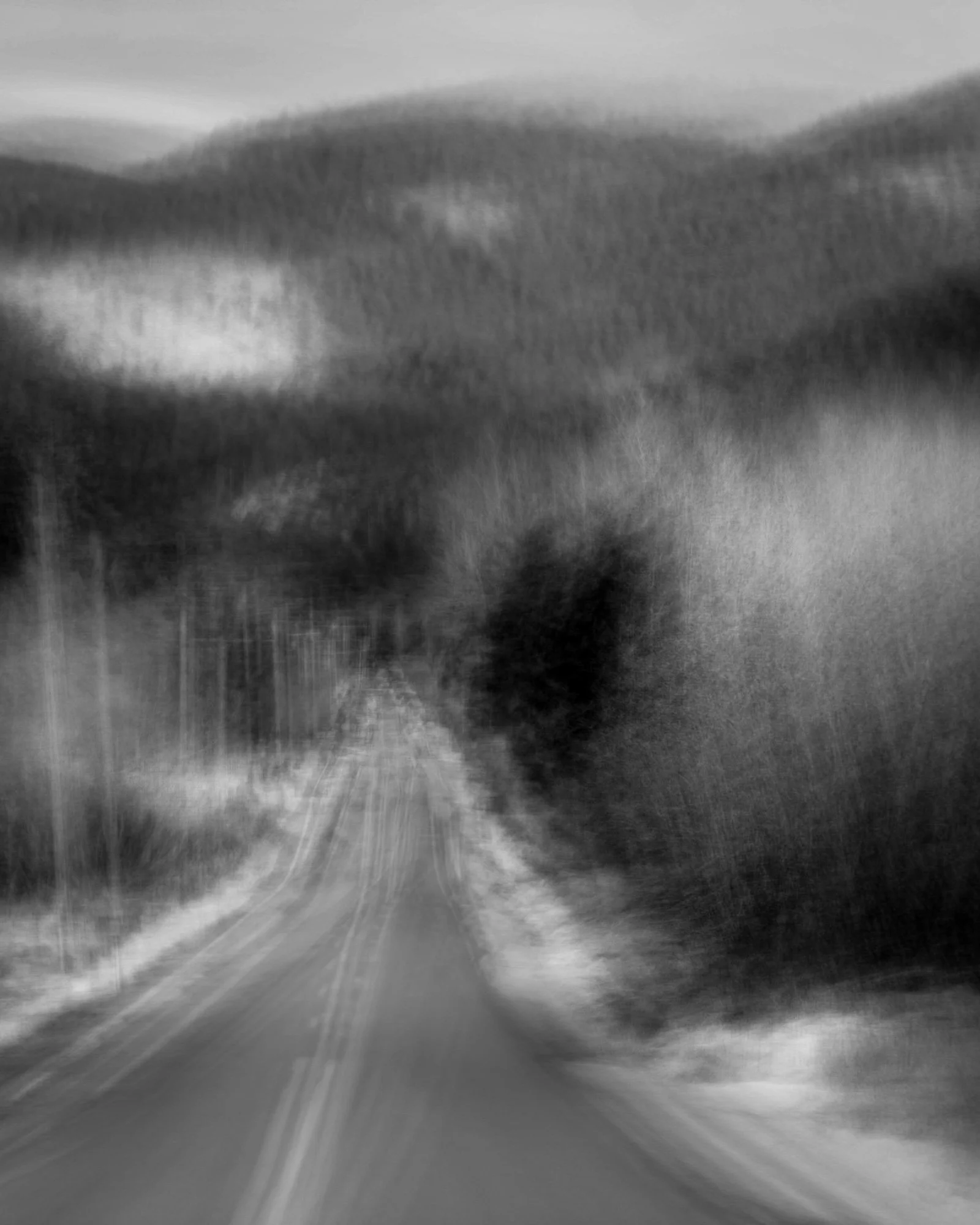 Black and white photo of a rural road with trees on both sides and cloudy sky.