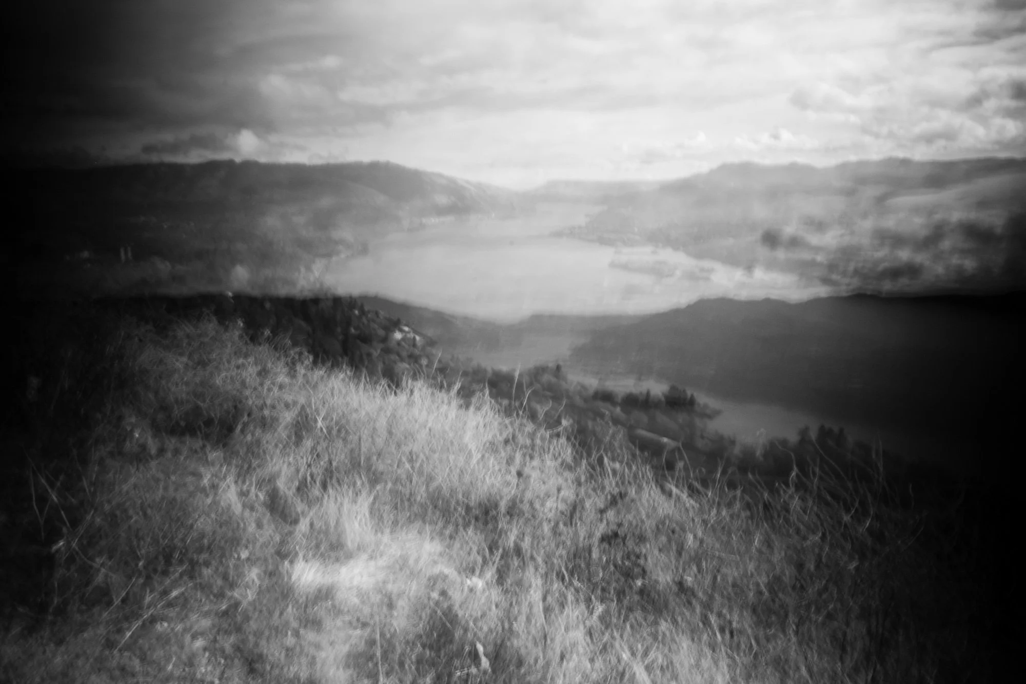 Black and white landscape view of a wide river or lake surrounded by hills and cloudy sky.