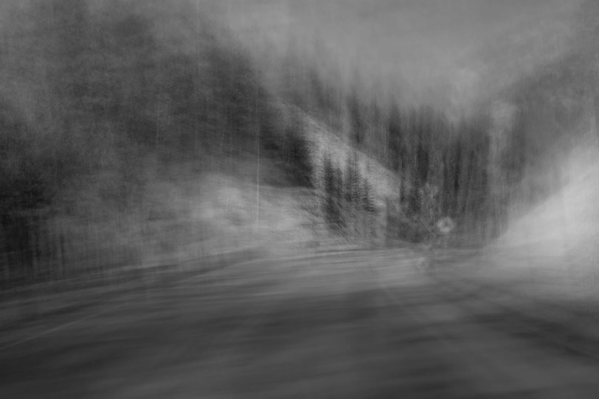 A blurry, black-and-white photo of a snow-covered or icy landscape with trees in the distance.