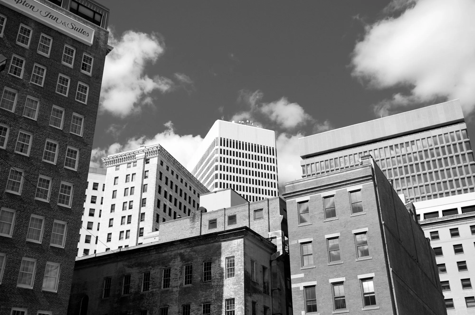 Black and white photo of tall city buildings with a partly cloudy sky.