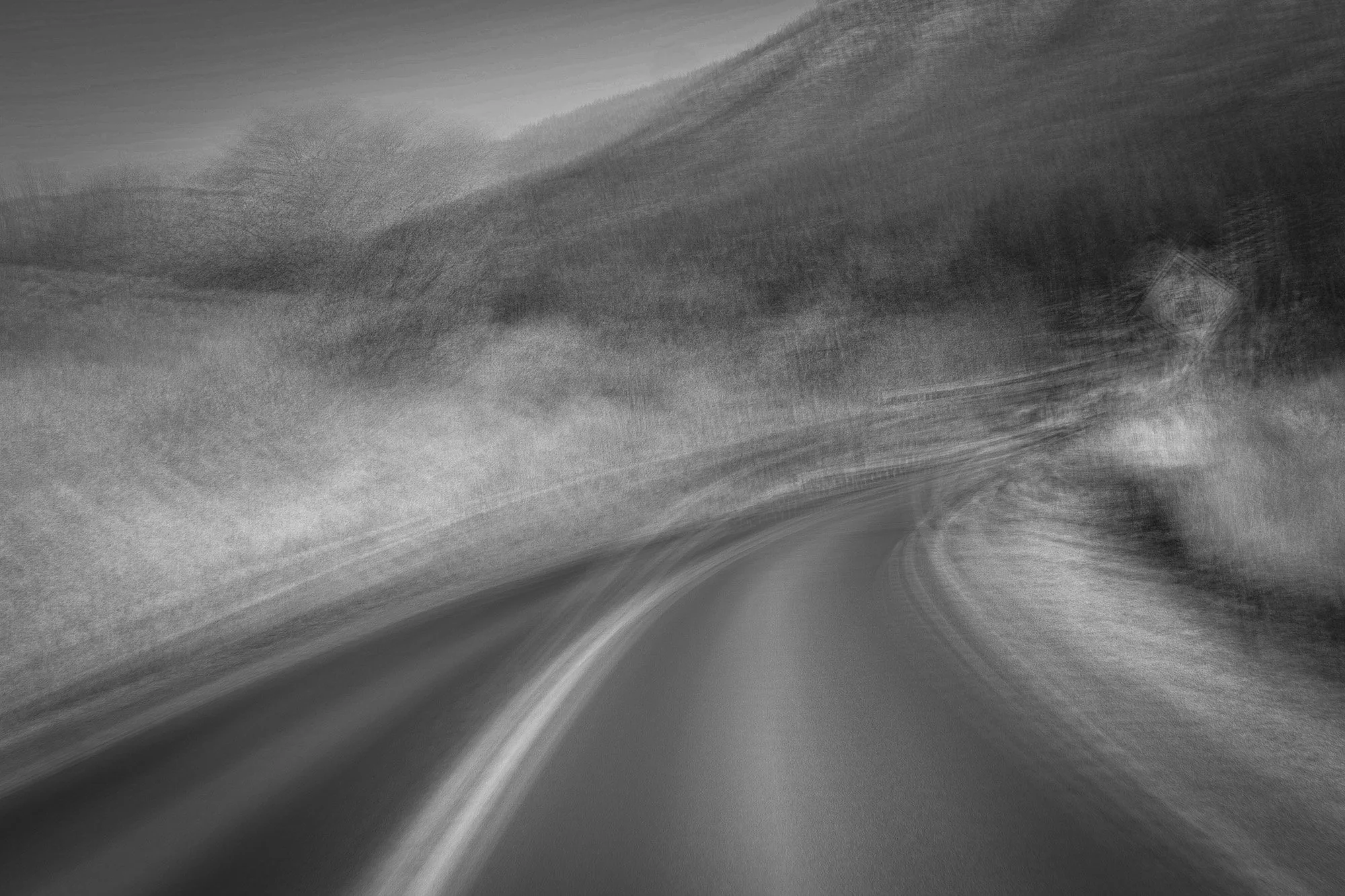 Black and white photo of a winding road running through a hilly landscape.
