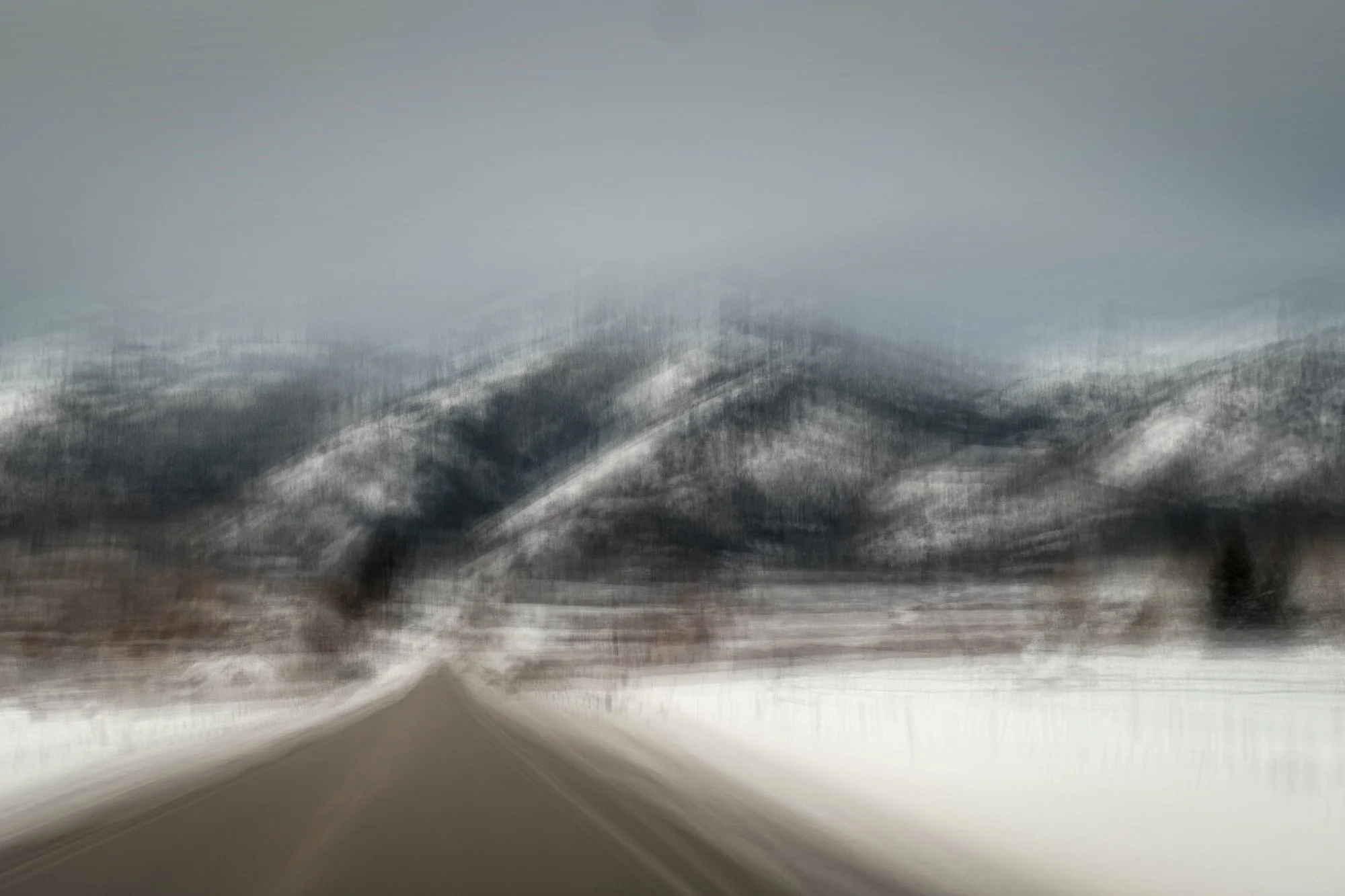 A snow-covered mountain landscape viewed from a blurred, moving perspective of a road.