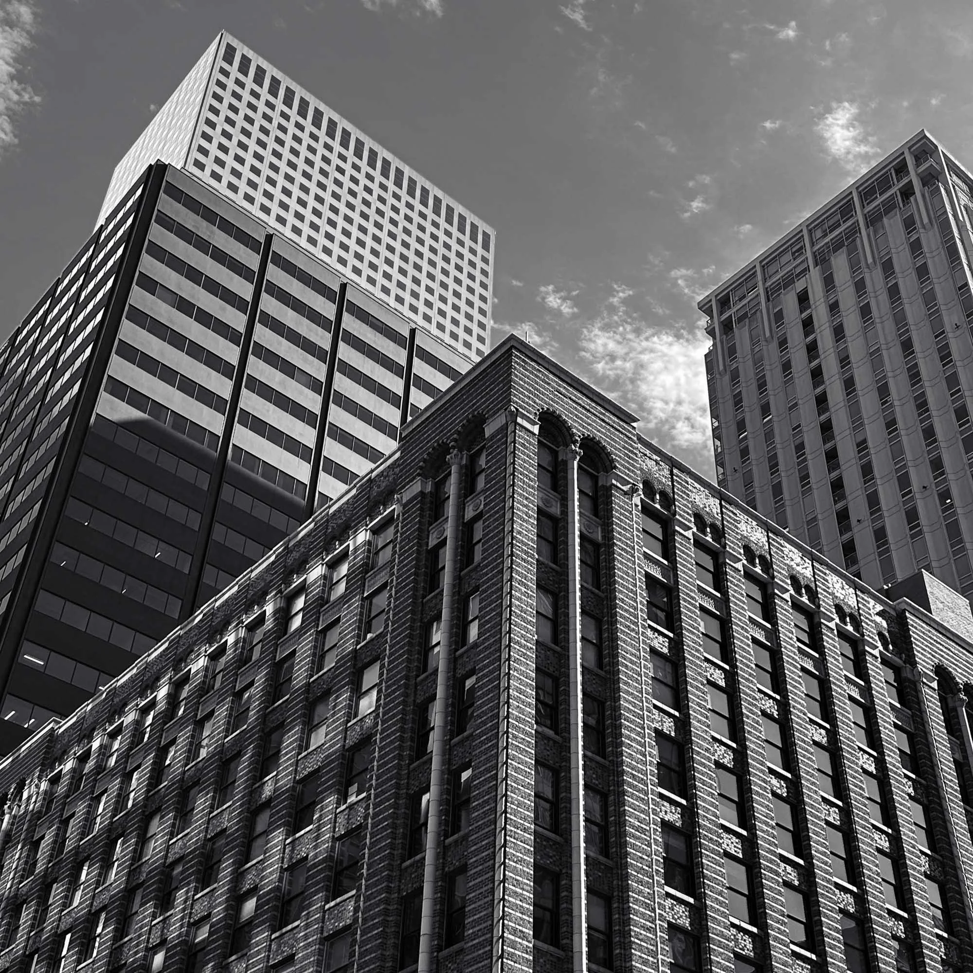 Black and white photo of tall city buildings with a cloudy sky in the background.