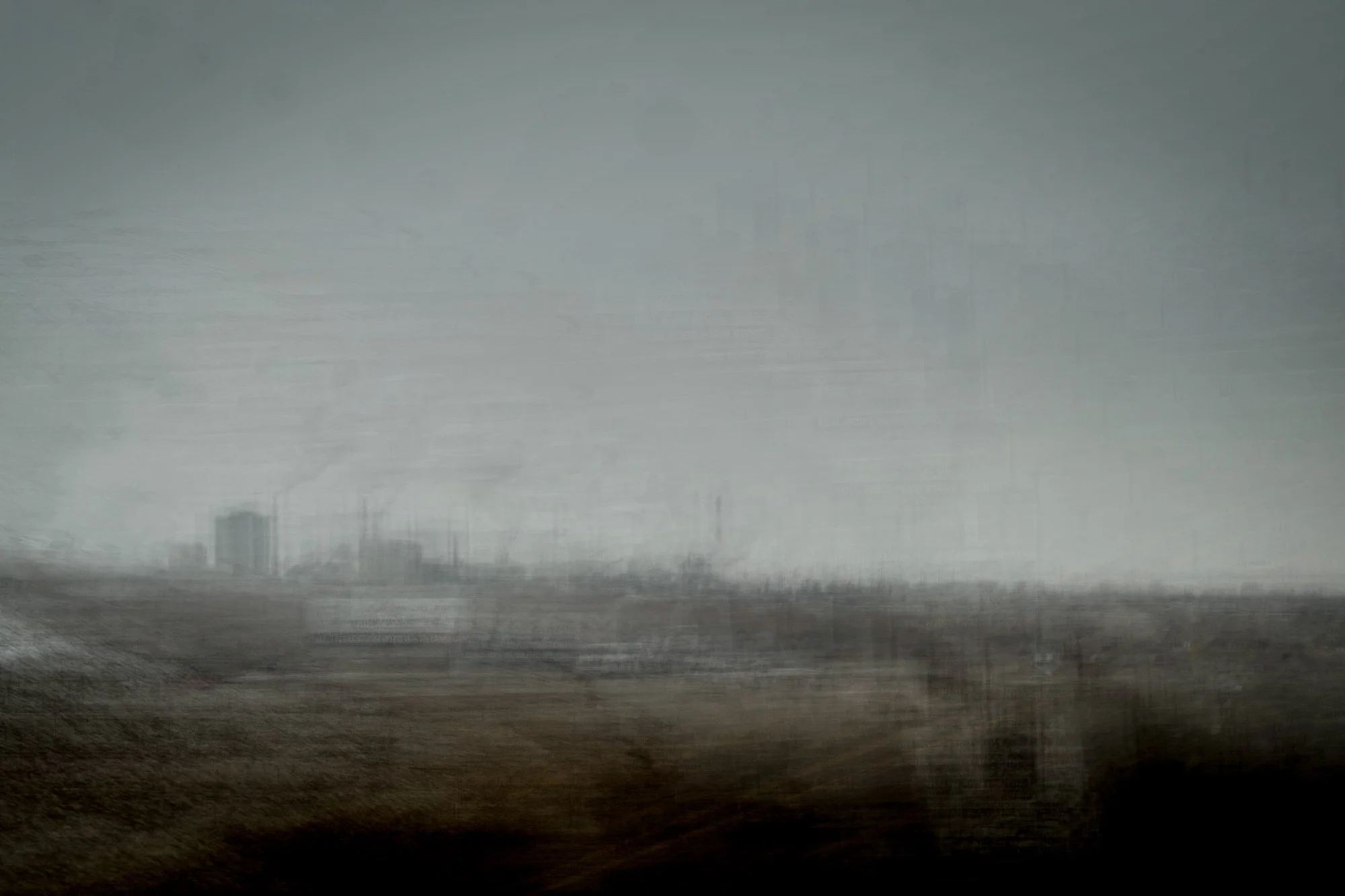 Blurred landscape with distant buildings under a cloudy sky, giving a sense of motion or foggy weather.