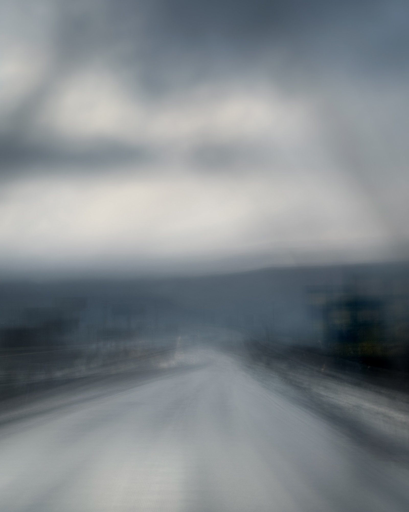Blurred view of a road under cloudy sky, possibly taken from a moving vehicle.
