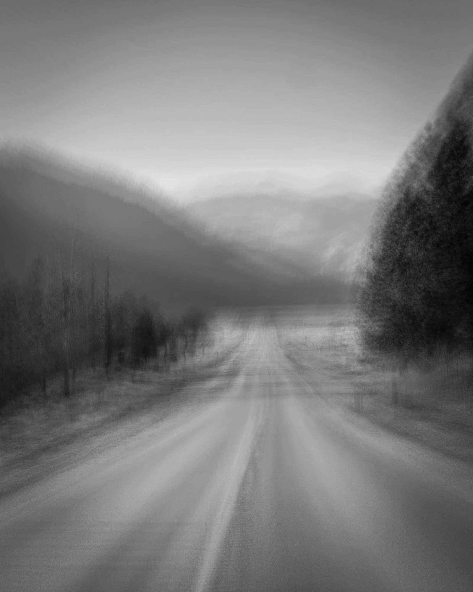 Black and white photo of a deserted road stretching into distant hills, blurred for artistic effect.