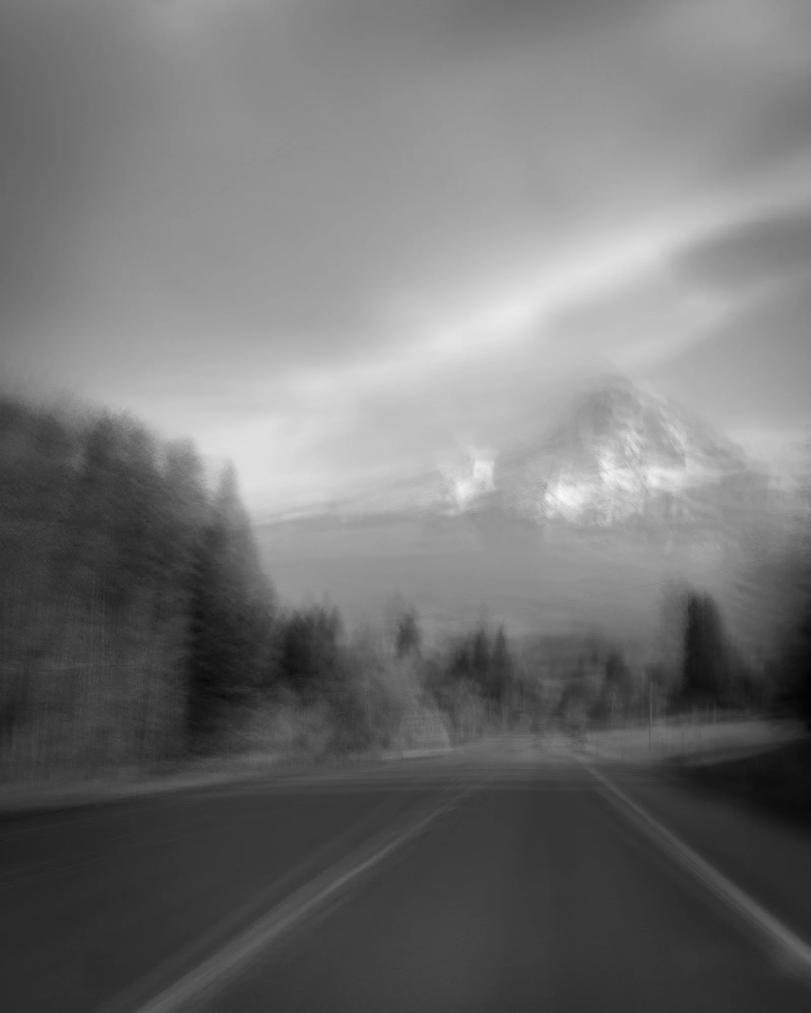 Black and white photo of a road leading towards mountains in the background with cloudy sky.
