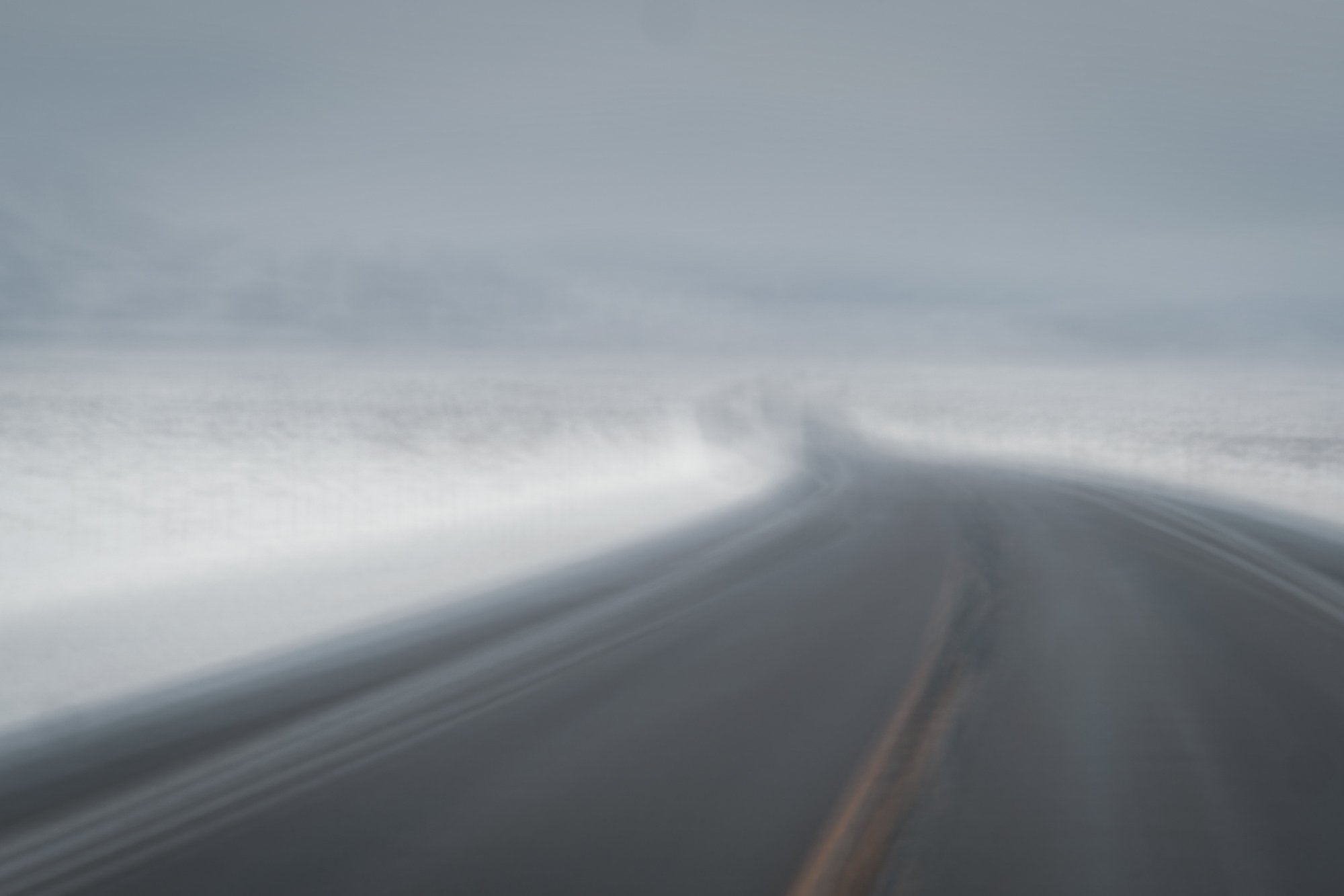 A snowy, icy highway with snow along both sides and a gray cloudy sky.