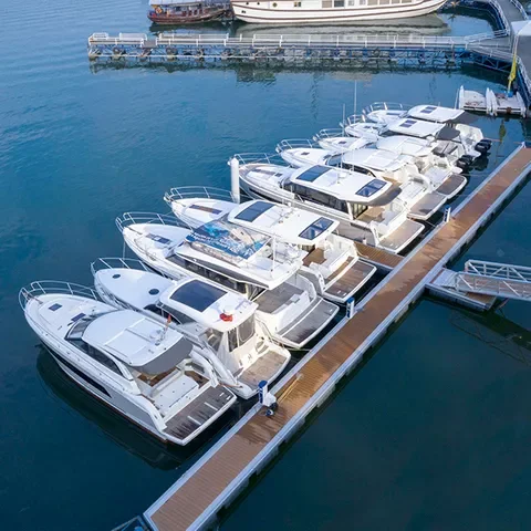 Multiple white yachts docked at a marina, moored along a wooden pier, with calm water surrounding them.