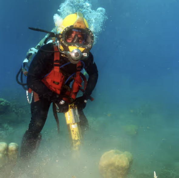 Scuba diver underwater near rocks with a yellow tank and full gear.