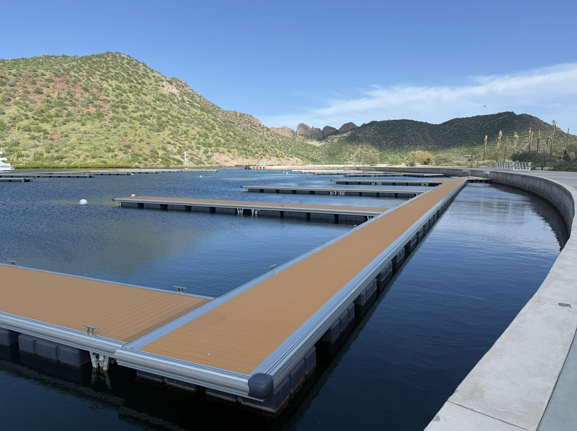 Empty floating boat docks on turquoise water with a few boats and green hills in the background under a partly cloudy sky.
