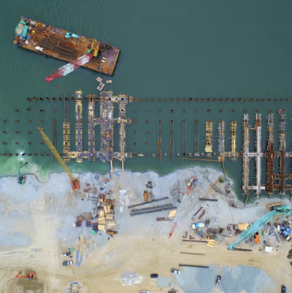 Aerial view of a construction site on a beach, with numerous docked boats and floating structures in the water.