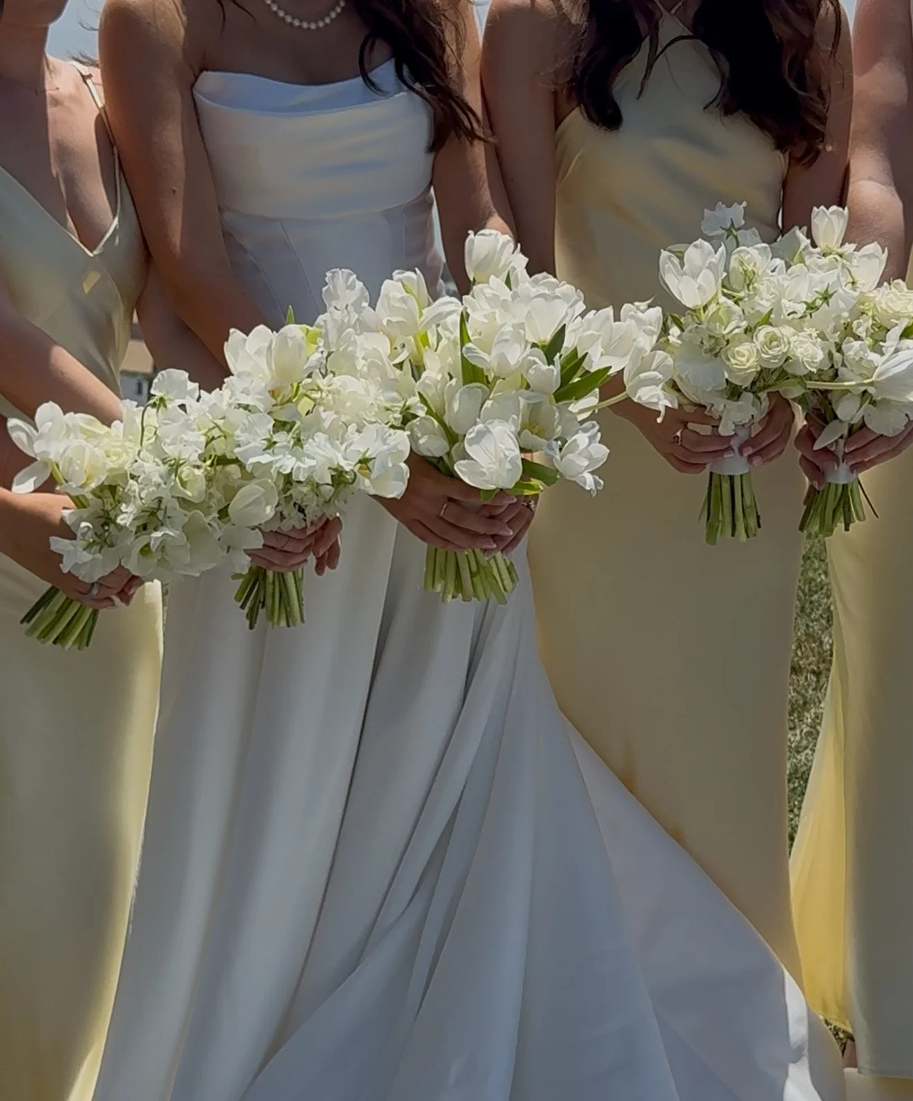 A group of women dressed in pastel-colored dresses holding white flower bouquets, likely at a wedding or special ceremony.