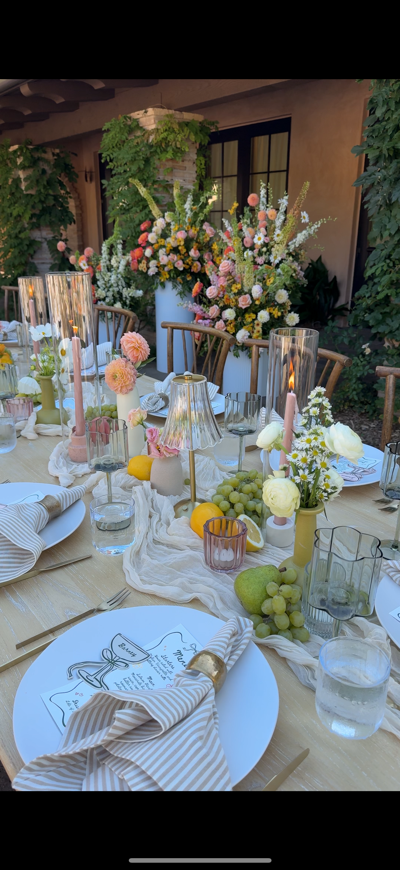 Decorative outdoor table set for a celebration with floral arrangements, candles, and place settings.