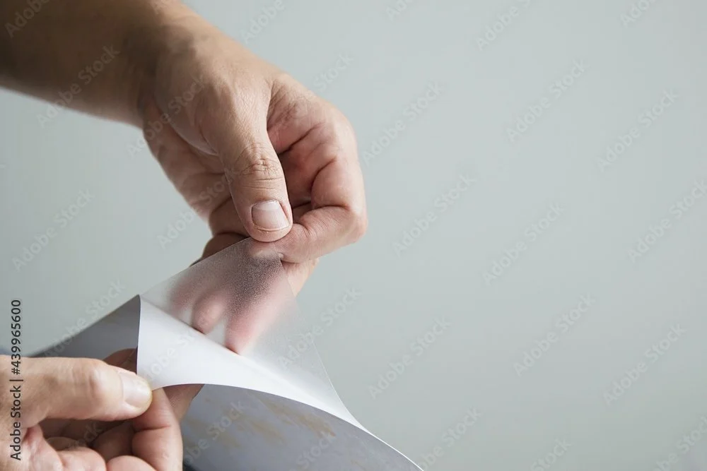 Hands peeling a white sheet of paper off a gray background.