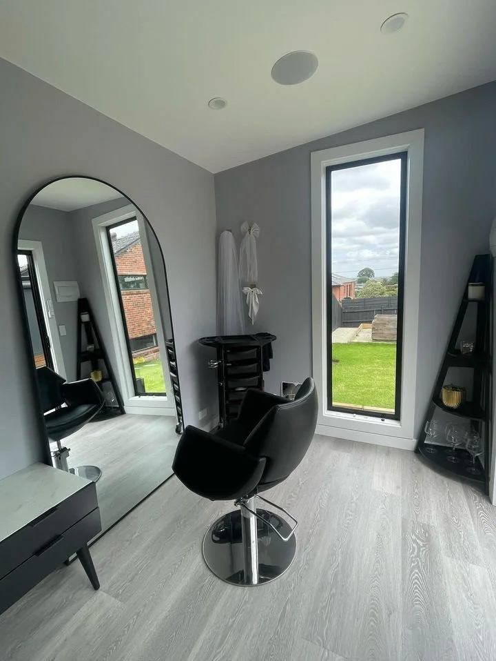 Modern hair salon chair in front of a large mirror, with window showing a green lawn and cloudy sky outside.