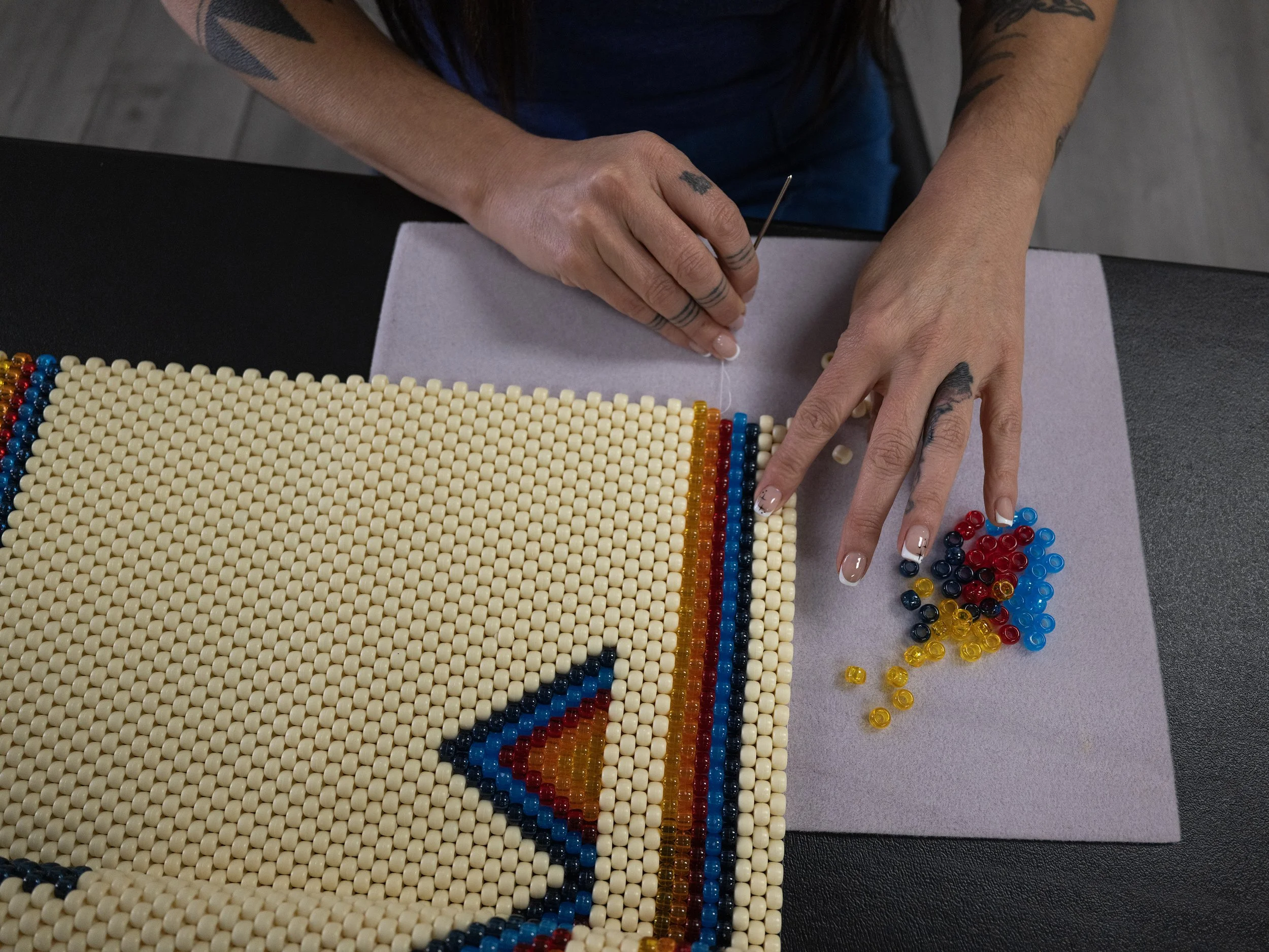 Person working with colorful beads on a black surface, threading beads onto a string, with beads spilling around.