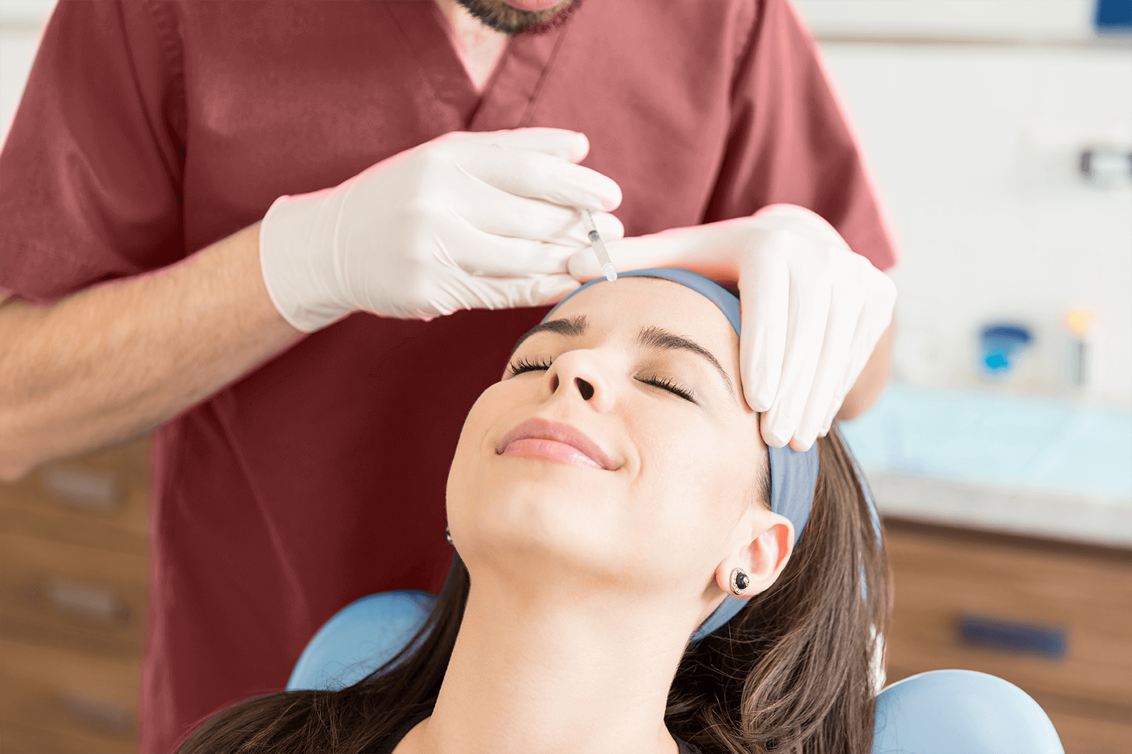 A woman receiving a Botox injection in her forehead from a healthcare professional wearing gloves in a clinical setting.